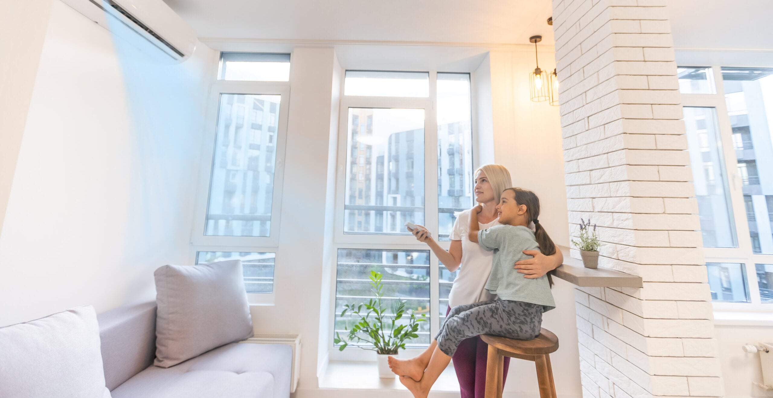 Happy family under air conditioner, mom holding remote control switch on conditioning in living room adjust comfort temperature for daughter, climate system at modern home